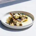 Rotzungenfilets mit Blumenkohl, grünen Oliven, Kapern und Petersilie auf einem hellen Teller