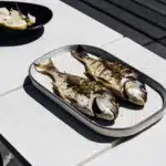 Gegrillte Doraden mit Zitronenscheiben und Kräutern auf einer Servierplatte