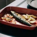 Ofenmakrele mit Zitronenscheiben, Petersilie und goldbraunen Bratkartoffeln auf einem Teller