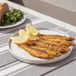 Goldbraun frittierte Sardinen mit Zitronenspalten auf einem Teller