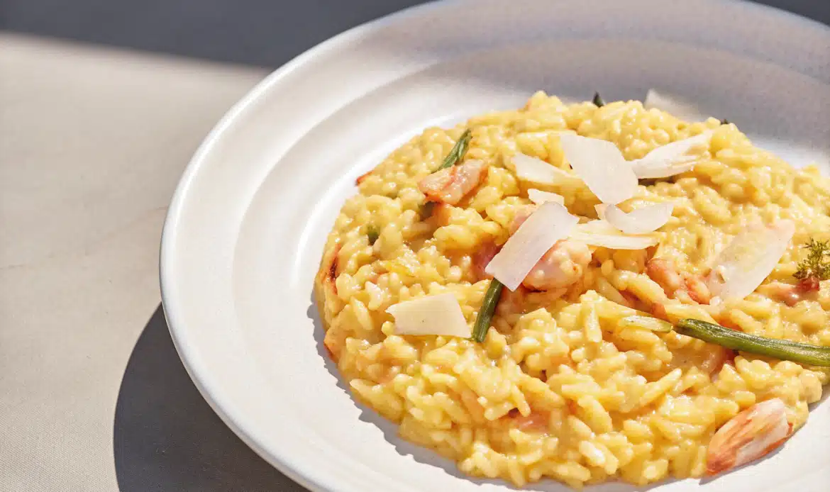Cremiges Risotto mit Lachs, Garnelen, grünem Spargel, Zitrone und Parmesan auf einem weißen Teller