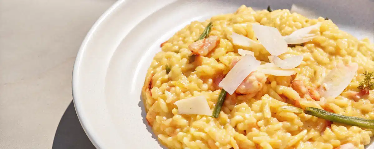 Cremiges Risotto mit Lachs, Garnelen, grünem Spargel, Zitrone und Parmesan auf einem weißen Teller