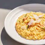 Cremiges Risotto mit Lachs, Garnelen, grünem Spargel, Zitrone und Parmesan auf einem weißen Teller