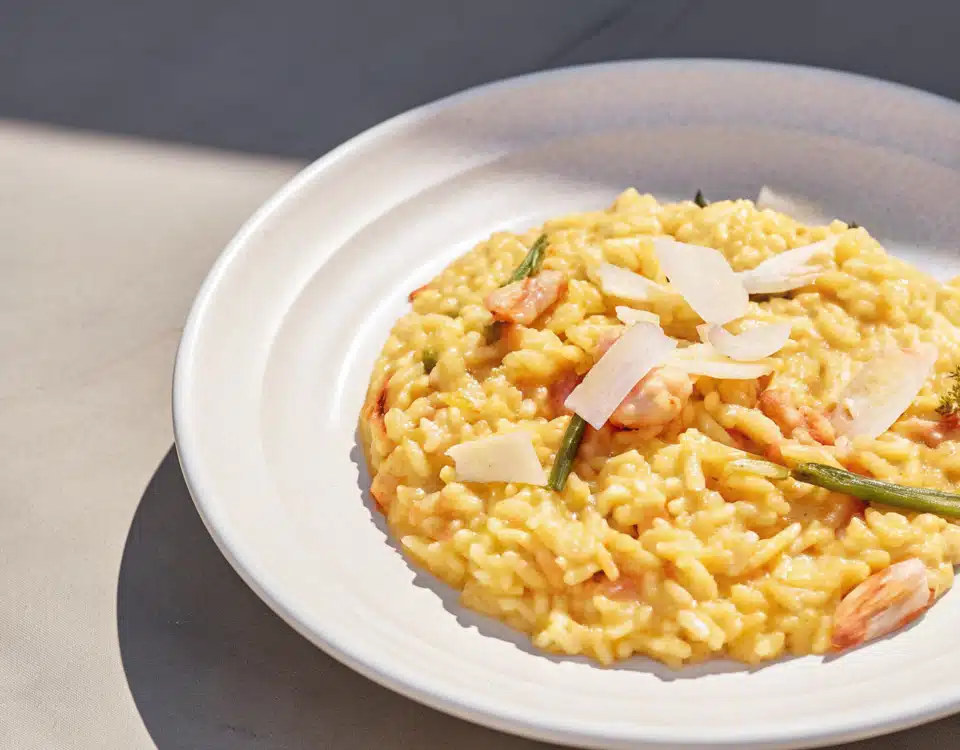 Cremiges Risotto mit Lachs, Garnelen, grünem Spargel, Zitrone und Parmesan auf einem weißen Teller